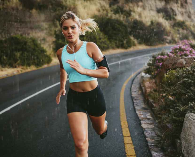 vrouw met lang blond haar die aan het hardlopen is op de openbare weg met oortjes, een blauw topje en short