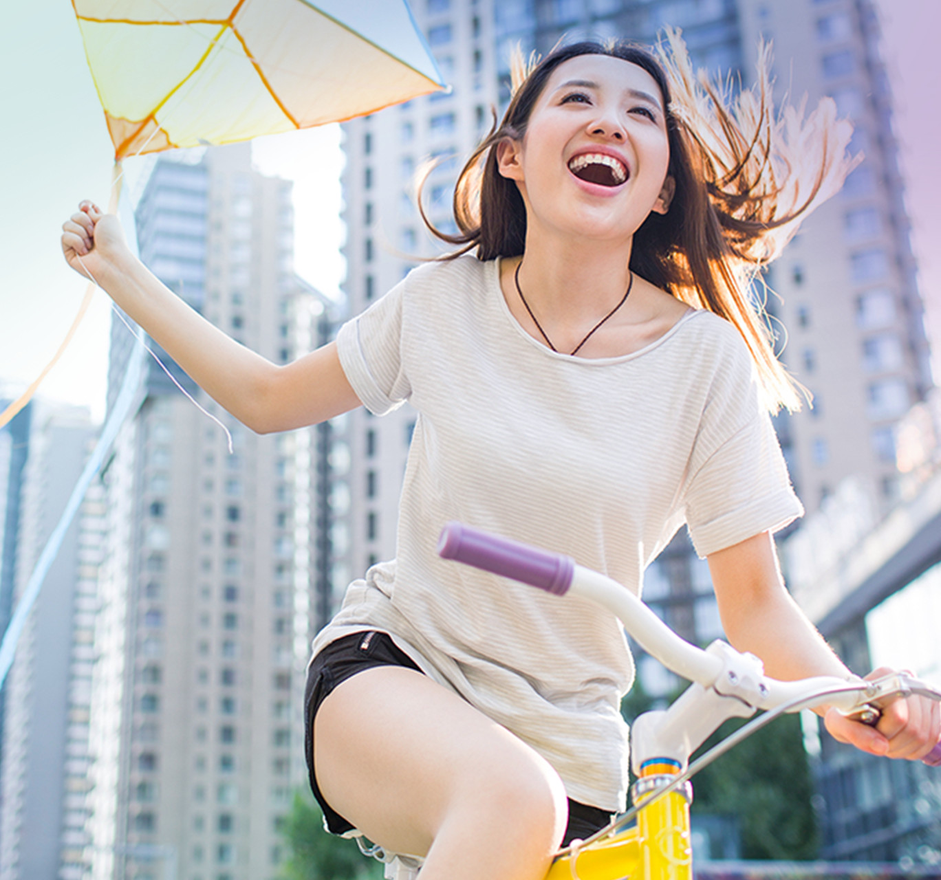 Jeune femme qui fait du vélo dans une grande ville en tenant un cerf-volant.