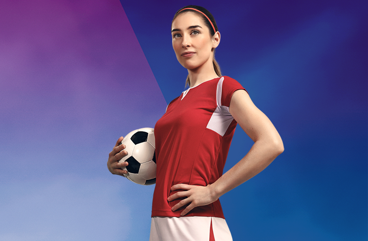 aktive junge Frau, die einen Fussball hält und ein Fussballtrikot trägt