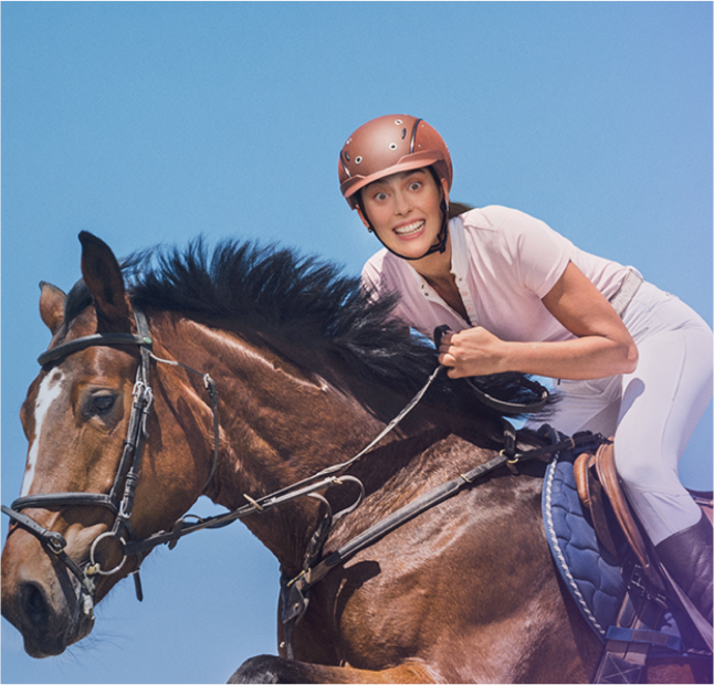 Žena jedoucí na tmavě hnědém koni se vzrušujícím výrazem na tváři, která nosí hnědou helmu, růžové tričko s krátkým rukávem, bílé kalhoty a tmavě hnědé boty.