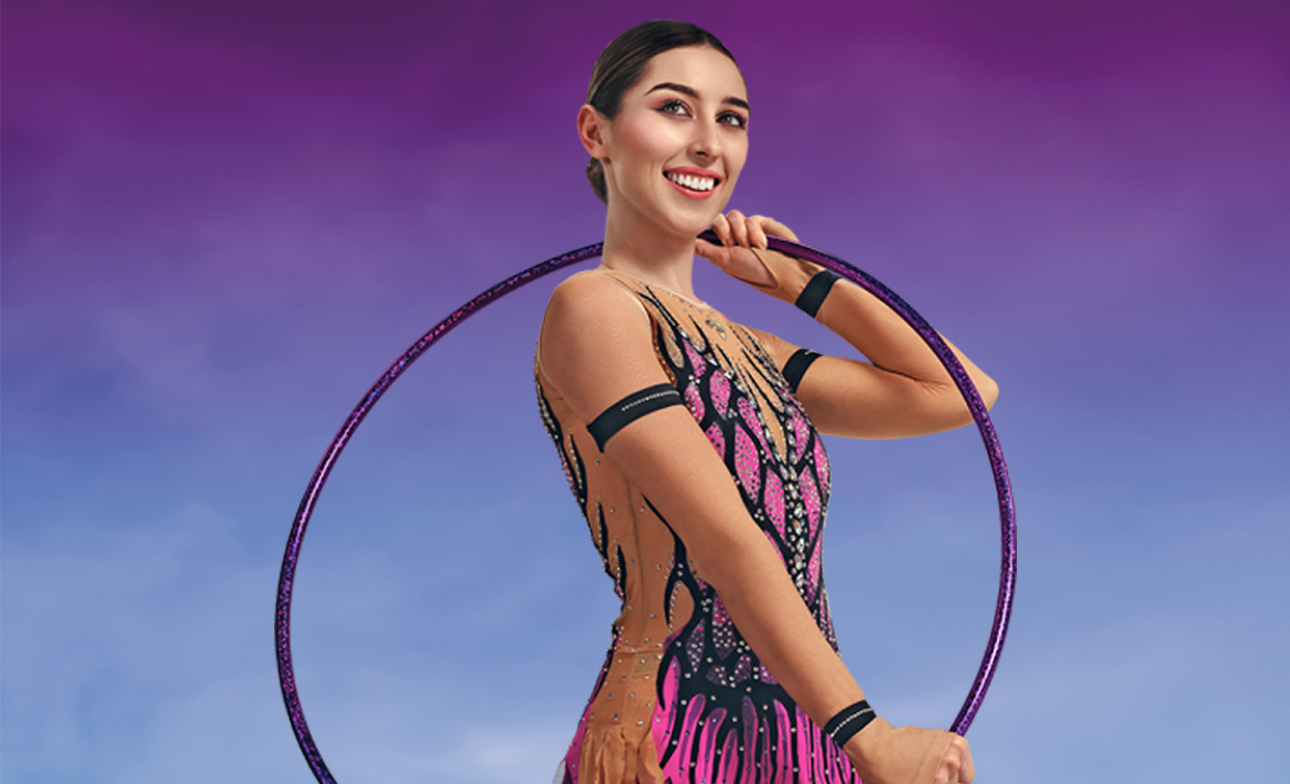smějící se mladá žena s kruhem na aerobik kolem svého těla, která nosí růžovo-černý kostým pro gymnastky