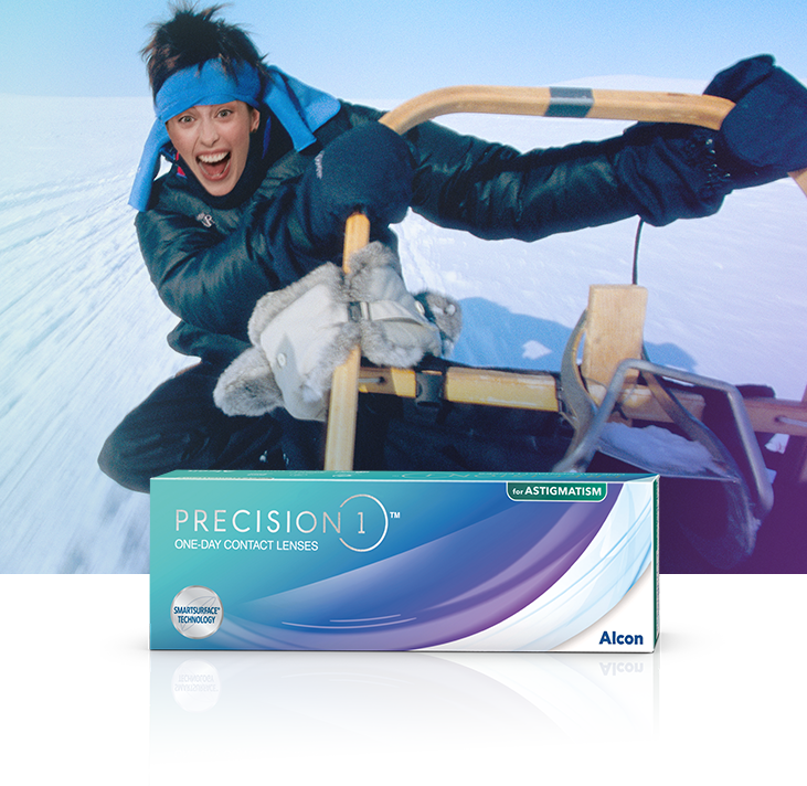 Mujer con diadema azul y abrigo de invierno paseando en trineo sobre la nieve con lentes de contacto diarias Precision1 para astigmatismo, caja de producto en primer plano