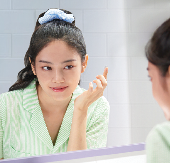 Young woman looking in mirror while putting in contact lens