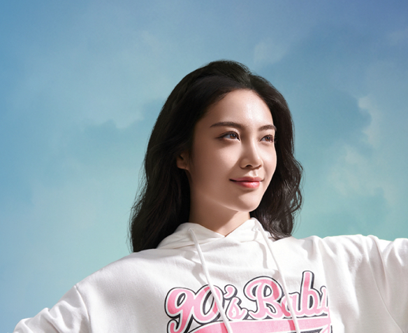 Young woman looking off into the distance smiling while wearing a white hooded sweatshirt reading, 90s Baby