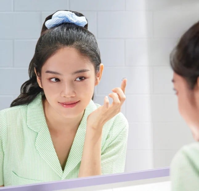 Young woman looking in mirror while putting in contact lens