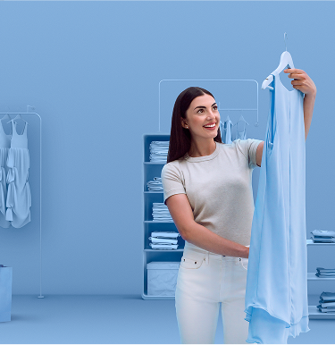 Usměvavá mladá žena drží světle modré šaty v elegantním šatníku, oblečená v ležérním stylu a užívající si okamžik, odrážející sebevědomý a moderní životní styl.
